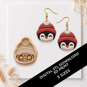 Puede incluir: Un par de pendientes con forma de pingüino con gorros de invierno rojos y blancos y un cortador de galletas de plástico beige a juego. El texto dice DIGITAL STL DOWNLOAD 3D PRINT 3 SIZES. Los pendientes tienen ganchos de metal dorado.