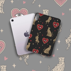 May include: A black phone case featuring a repeating pattern of cheetahs, red heart-shaped eyes, and small red hearts. A white tablet with the Apple logo is next to the phone case.