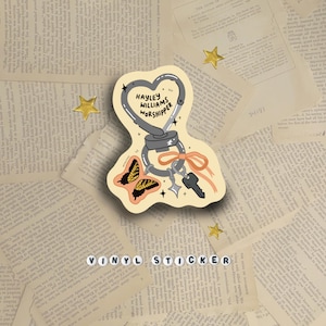 May include: A vinyl sticker with a heart-shaped design, a carabiner, keys, and a butterfly illustration. The text "HAYLEY WILLIAMS WORSHIPPER" is on the heart. The sticker is set against a backdrop of vintage book pages, with gold star accents.