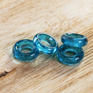 May include: Four turquoise glass rings, stacked on a wooden surface. The rings are smooth and have a slightly iridescent finish.