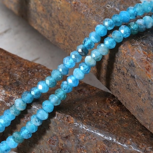 May include: A strand of blue gemstone beads, likely aquamarine, with a faceted finish. The beads are strung on a clear thread and are arranged in a double row.