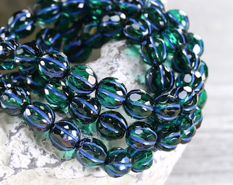 May include: Close-up of a strand of faceted beads. The beads are a deep emerald green with a blue stripe. The beads are arranged in a circular pattern, suggesting a bracelet or necklace.