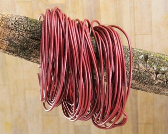 May include: A spool of burgundy leather cord, wrapped around a branch. The cord is smooth and shiny, and appears to be of high quality.
