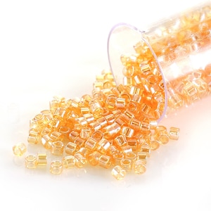 May include: A clear plastic container filled with small, round, translucent orange beads. The beads are spilling out of the container onto a white surface.