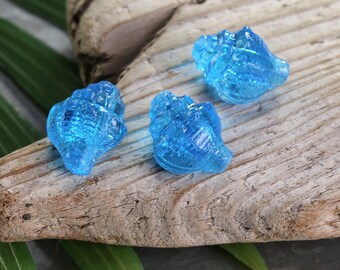 May include: Three blue glass seashells with a textured surface. The seashells are arranged on a piece of driftwood.
