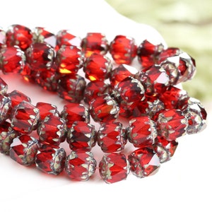 May include: A strand of red glass beads with a faceted, starburst design. The beads have a silver-toned metallic finish.
