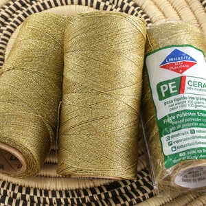 May include: Three spools of gold metallic thread, each wrapped in brown paper with the brand name "Linhasita" printed on the label. The label also includes the text "PE Cera 100% Polyester" and "Fia de Poliester Encerado" in Portuguese.