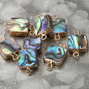 May include: A group of eight square-shaped iridescent abalone shell connector charms with gold-toned metal loops. The charms have a blue, green, and gold color scheme.