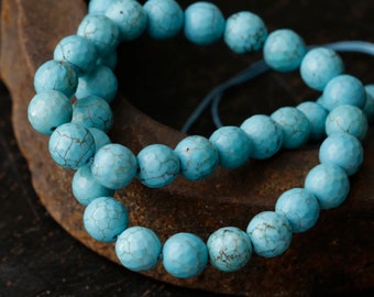 May include: A double strand of turquoise beads, each bead is a light blue color and has a slightly rough texture. The beads are strung on a thin cord and are arranged in a circular pattern.