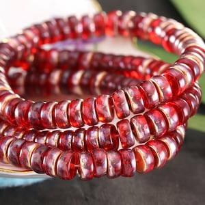 May include: A strand of red glass beads with gold accents. The beads are round and have a slightly iridescent finish.
