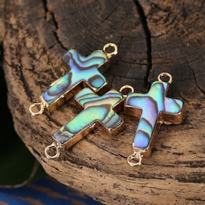 May include: Three iridescent abalone shell cross charms with gold-toned metal accents. The charms have a blue, green, and purple iridescent sheen.