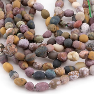 May include: Strands of natural stone beads in various colors, including shades of brown, purple, yellow, and gray. The beads are oval-shaped and strung together, showcasing a variety of textures and patterns. The beads are approximately 1 cm in length.