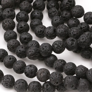 May include: Close-up of black lava rock beads. The beads are round with a porous texture. The beads are strung together, creating a necklace or bracelet. The beads are a dark charcoal color.