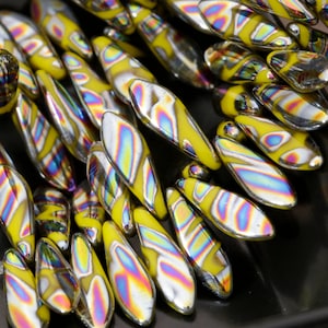 May include: A close-up of iridescent glass beads with yellow and silver patterns. The beads are shaped like teardrops and are arranged in a fan shape.