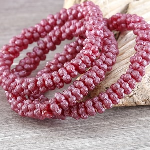 May include: A close-up of a strand of deep red beads. The beads are small and round, and they are arranged in a spiral pattern. The beads are made of a shiny material, and they reflect the light.