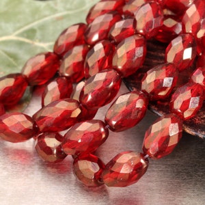May include: A strand of red faceted glass beads. The beads are oval shaped and have a metallic sheen.