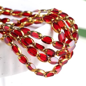 May include: A strand of red and gold oval-shaped beads. The beads are strung together on a clear thread. The beads are arranged in a random pattern.