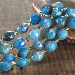 May include: A strand of blue gemstone beads with a faceted finish. The beads are strung on a wire with gold-colored spacer beads.