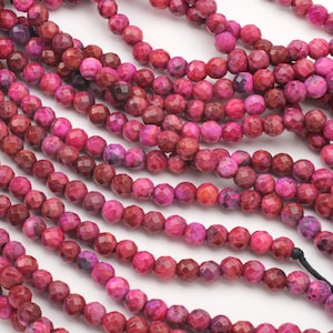 May include: A strand of pink agate beads with a faceted finish. The beads are approximately 6mm in diameter and have a natural, marbled appearance.