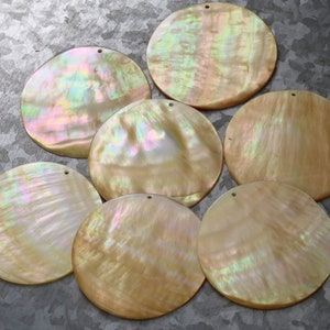 May include: Seven iridescent round mother of pearl shell discs with a hole in the center. The shells are various shades of cream, white, and gold.