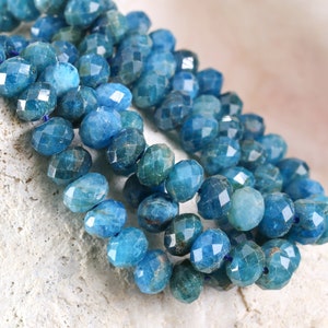 May include: A strand of faceted blue apatite beads. The beads are a light blue color and have a faceted, or cut, surface. The beads are strung together on a clear thread.
