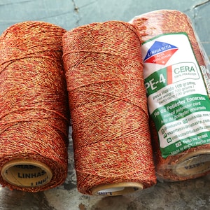 May include: Three spools of orange and gold waxed polyester cord. The label reads "Linhasita Alta Qualidade PE-4 Cera 100% Poliester. Peso liquido 100 gramas / Net weight 100 grams / Peso neto 100 gramos. Fio de Poliester Encerado / Waxed polyester cord / Hilo de Poliester encerado. Linhasita.com.br. Exportacao@linhasita.com.br. Linhasita@linhasita.com.br. Feito no Brasil / Made in Brazil / Hecho en Brasil."