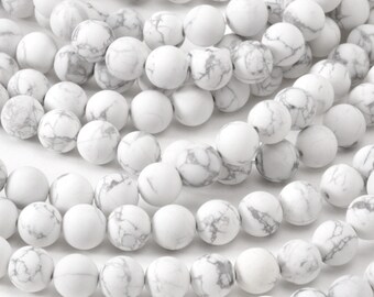 May include: A strand of white howlite beads with a marbled pattern. The beads are round and smooth, and they are strung on a clear thread.
