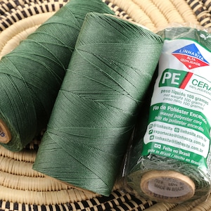 May include: Three spools of dark green waxed polyester thread. The spools are labeled "Linhasita Alta Qualidade PE Cera 100% Poliéster" and "Feito no Brasil".