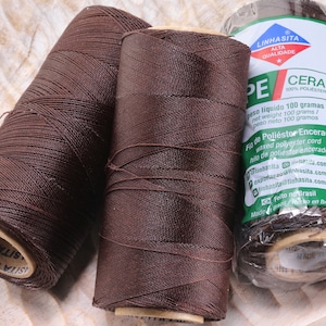 May include: Two spools of brown waxed polyester cord, each weighing 100 grams. The spools are labeled "Linhasita Cera 100% Polyester" and "Made in Brazil".