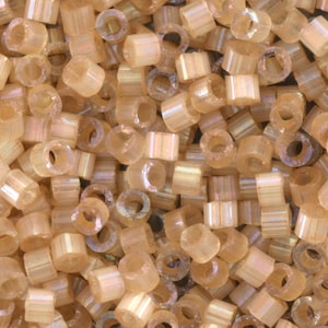 May include: A close-up shot of a pile of small, cylindrical beads. The beads are a translucent, light amber color with a subtle iridescent sheen. Each bead has a hole running through the center, and they are scattered randomly.