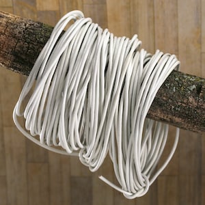 May include: A white cord wrapped around a weathered wooden branch. The cord is coiled and ready to be used.