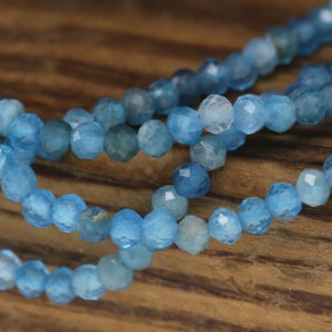 May include: A strand of blue gemstone beads with a faceted finish. The beads are strung on a clear thread and are arranged in a circular pattern.