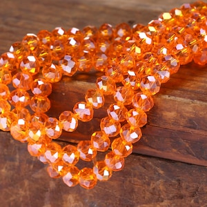 May include: A strand of orange faceted glass beads. The beads are strung together on a clear thread and are arranged in a loose, flowing pattern.