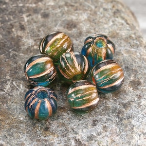 May include: A group of eight round glass beads with a teal blue and gold color scheme. The beads have a textured surface and are arranged in a cluster.