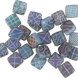 May include: A collection of 18 iridescent blue glass square beads with white geometric patterns. The beads are approximately 1 cm in size.