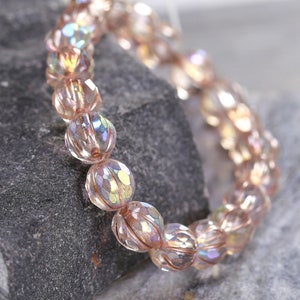 May include: A pink iridescent beaded bracelet with faceted glass beads. The bracelet is made of many small round beads that are strung together.