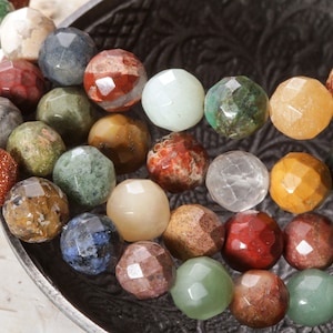 Peut inclure: Un brin de perles de pierres précieuses facettées colorées. Les perles sont de différentes nuances de vert, rouge, marron, jaune et bleu. Les perles sont disposées en cercle sur un fond sombre.
