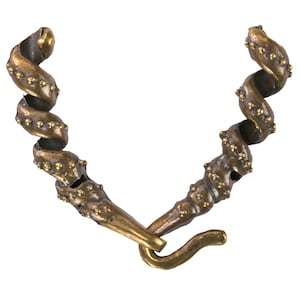 May include: A bronze-colored necklace with a spiral design. The necklace features a hook clasp and is adorned with small, gold-colored studs along the spiral. The design is reminiscent of a sea creature or a stylized organic form.