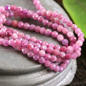 May include: A strand of pink faceted gemstone beads. The beads are round and have a smooth, polished finish.