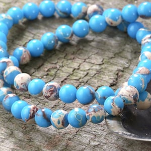 May include: A strand of blue and white marbled round beads. The beads are strung on a clear thread and are arranged in a circular pattern.