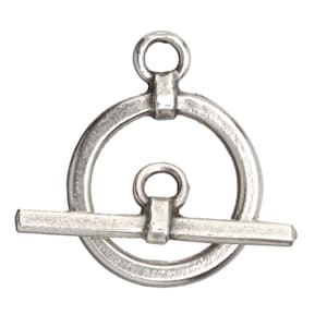 May include: A silver-toned toggle clasp, featuring a circular ring with a smaller ring at the top and a horizontal bar. The clasp is designed for jewelry making and has a vintage or antique appearance.