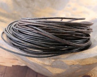 May include: A coiled bundle of dark brown, round leather cord. The cord has a smooth, matte texture and is wound into a circular shape, showing multiple layers of the thin, flexible material stacked together in a dense, continuous loop.