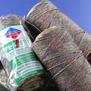 May include: Three spools of colorful waxed polyester cord, each with a label that reads "Linhasita Alta Qualidade PE-4 Cera 100% Poliester Encerado". The cord is a mix of blue, green, pink, and gold threads.