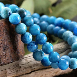 May include: A close-up of a beaded bracelet featuring large, round, blue beads. The beads have a marbled appearance with varying shades of blue. The bracelet is resting on a piece of wood.