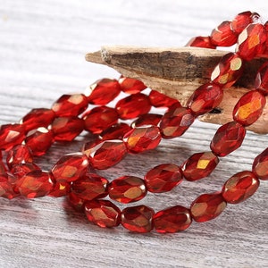 May include: A strand of red faceted glass beads. The beads are oval shaped and have a metallic sheen.