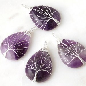 May include: Four amethyst gemstone pendants with silver wire wrapped around them in a tree design.
