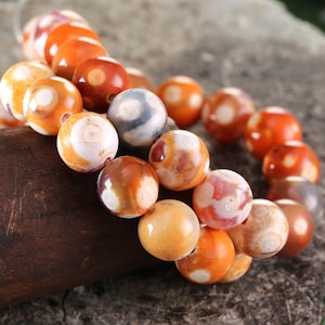 May include: A strand of agate beads in shades of orange, brown, and white. The beads have a swirling pattern and are strung on a clear cord.