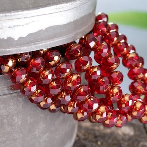 May include: A strand of red and gold glass beads in a metal container. The beads are faceted and have a shiny finish.