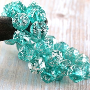 May include: A strand of turquoise blue glass beads with silver flecks. The beads are faceted and have a slightly irregular shape.