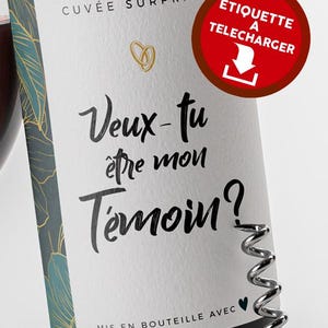 May include: A wine bottle with a label that reads "Veux-tu être mon Témoin?" in black script. The label also features the words "Cuvée Surprise" and a download icon. A silver corkscrew is partially visible.